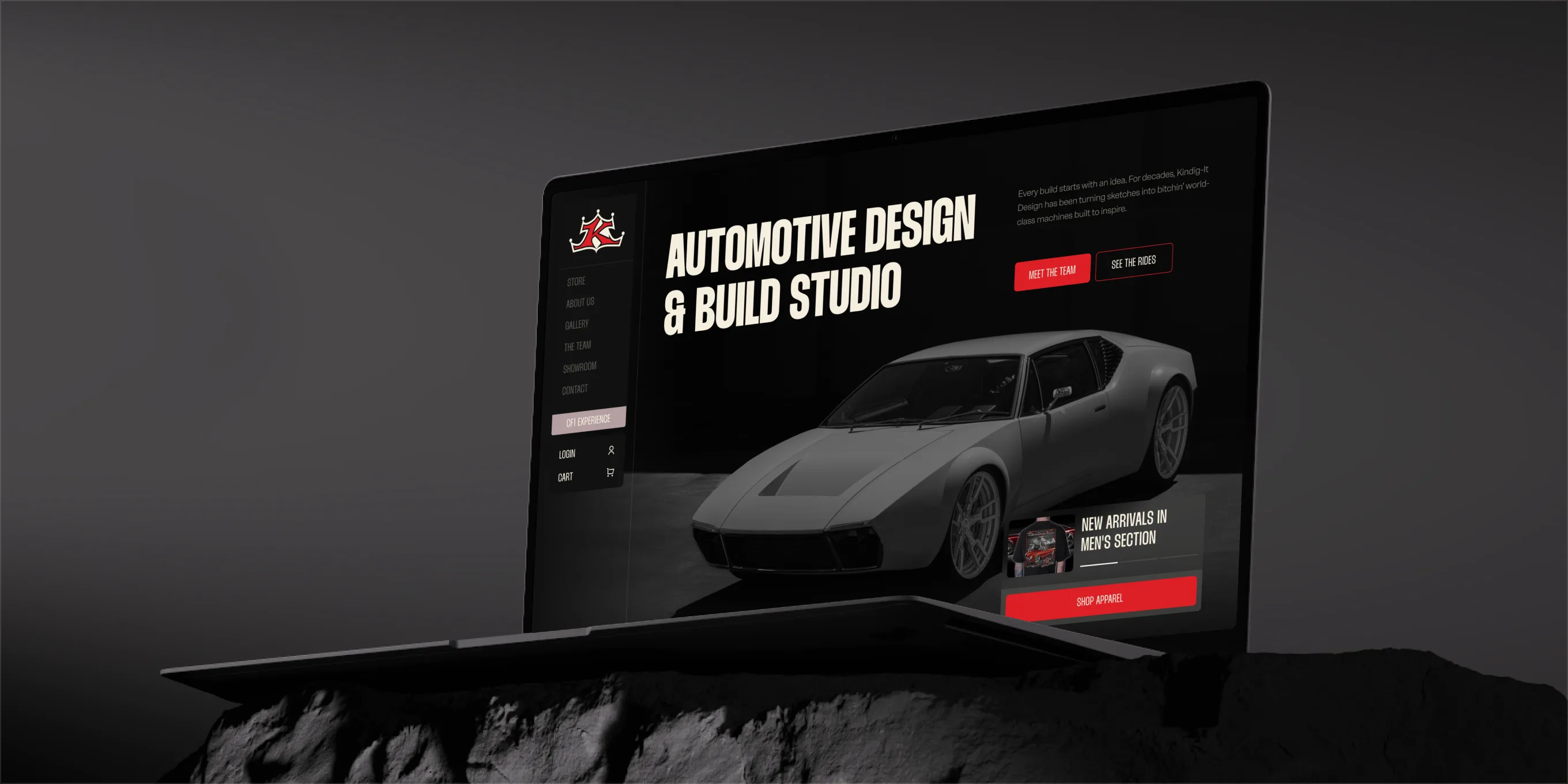 Laptop on a dark rock showing the Kindig-It homepage: Automotive Design & Build Studio with a silver custom car