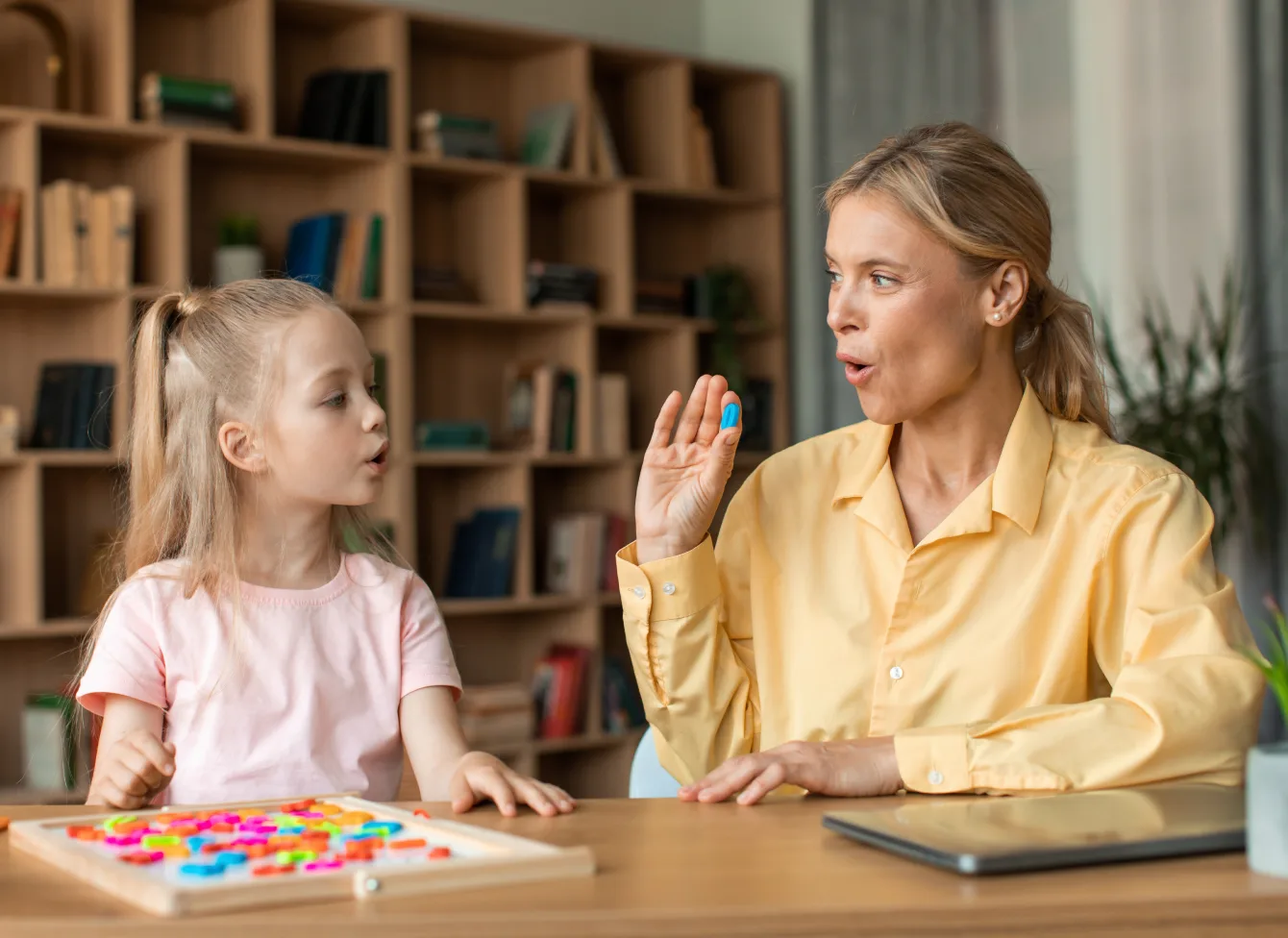 Speech therapist practicing sounds with a young girl at a table with a letter board